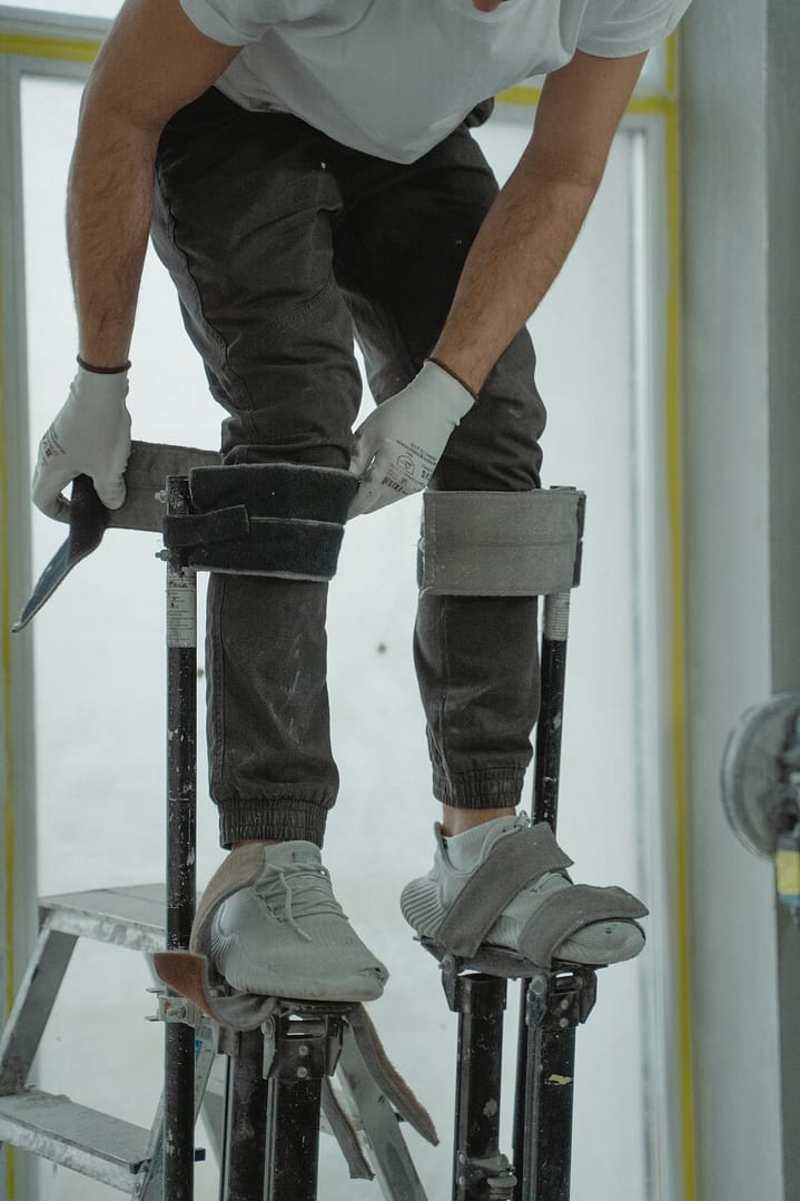 Construction worker on stilts in a house renovation project, using tools.